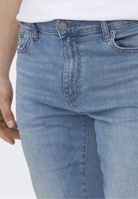 Ljusblå denimjeans med smal passform, med knäppning, fem fickor och subtil blekning längs benen.