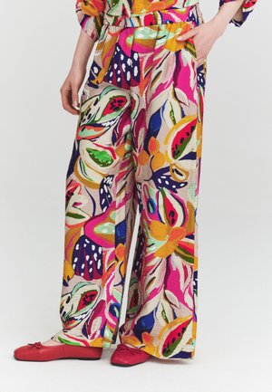 Pantalones de pierna ancha con estampado floral abstracto vibrante en rosa, naranja, verde y azul, combinados con un top a juego y bailarinas rojas.
