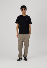 Svart t-skjorte med korte ermer og lite logo, kombinert med løstsittende beige cargobukser med sidelommer og svarte joggesko.
