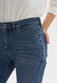 Tmavě modré džíny z denimu s úzkým střihem, s přední kapsou, viditelným šitím a zapínáním na kovový knoflík v pase.