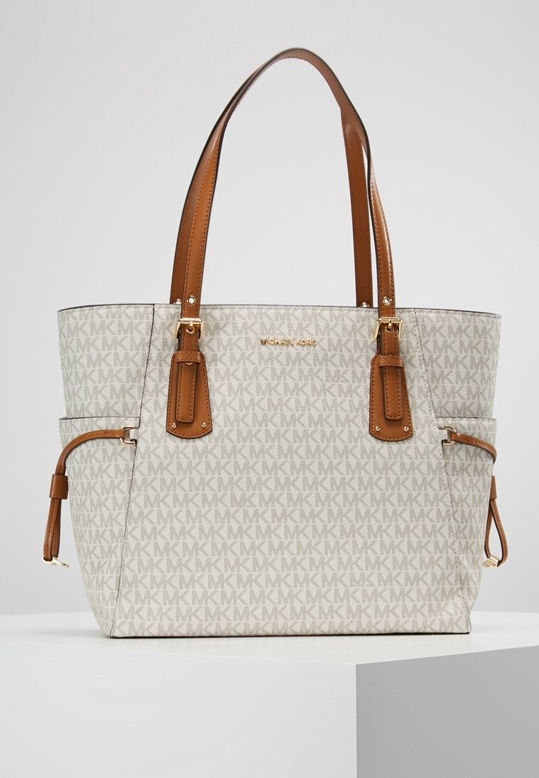 Sac fourre-tout beige et marron Michael Kors avec motif logo, doubles poignées en cuir marron, poches latérales et détails en métal doré.