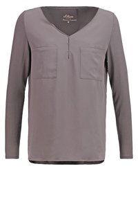 Blouse mauve à manches longues avec col en V, deux poches poitrine sur le devant, et un petit détail en encoche sous le col.