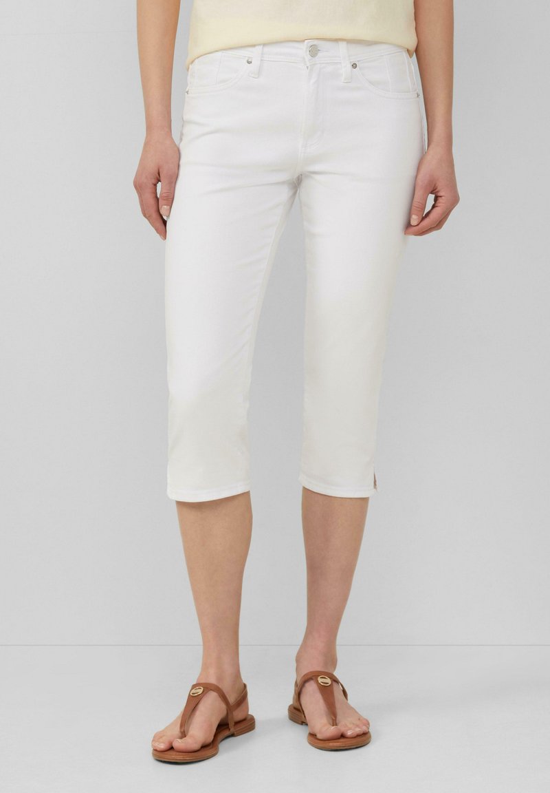 Pantalons capri en denim blanc avec une coupe droite, taille mi-haute et fentes latérales au bas. Associés à des sandales plates brunes.