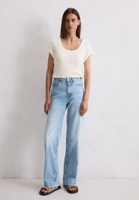 Jasny, prążkowany top z krótkim rękawem połączony z jasnoniebieskimi, wysokimi dżinsami o szerokich nogawkach oraz czarnymi sandałami na obcasie. Prosty, codzienny strój.