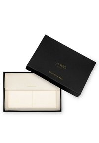 Crème portemonnee in een zwarte doos, met een klepafsluiting, twee buitenzakken en subtiele stikdetails. Gouden branding gedrukt op de voorkant.