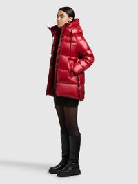 Czerwona kurtka puchowa z kapturem, o błyszczącej fakturze, z regulowanymi sznurkami i bocznymi kieszeniami. Noszona na czarnej spódnicy i rajstopach.