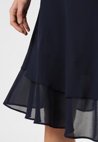 Navy blue layered dress featuring a soft, sheer fabric overlay with a flowing hemline. The bottom layer is more translucent.