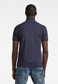 Námořnická polokošile s jednobarevným designem a krátkými rukávy, spojená se světlými modrými džíny s viditelným prošitím a dvěma zadními kapsami.