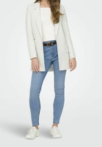 Lichtgekleurde blazer over een goed aansluitend wit topje, gecombineerd met lichtblauwe skinny jeans en witte sneakers. Heeft een bruine riem.