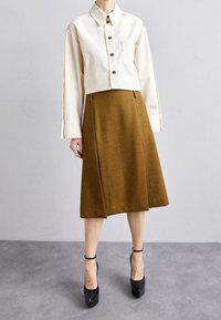 Avskuren krämfärgad skjorta med knappar, kombinerad med en brun herringbone-kjol i knähöjd och svarta plattformsskor, som visar upp skräddarsydd design och textur.