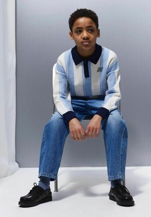 Gestreifter Pullover in Hellblau und Weiß mit einem dunklen Kragen, kombiniert mit blauen Jeans und schwarzen Schnürschuhen. Schlichtes, lässiges Design.