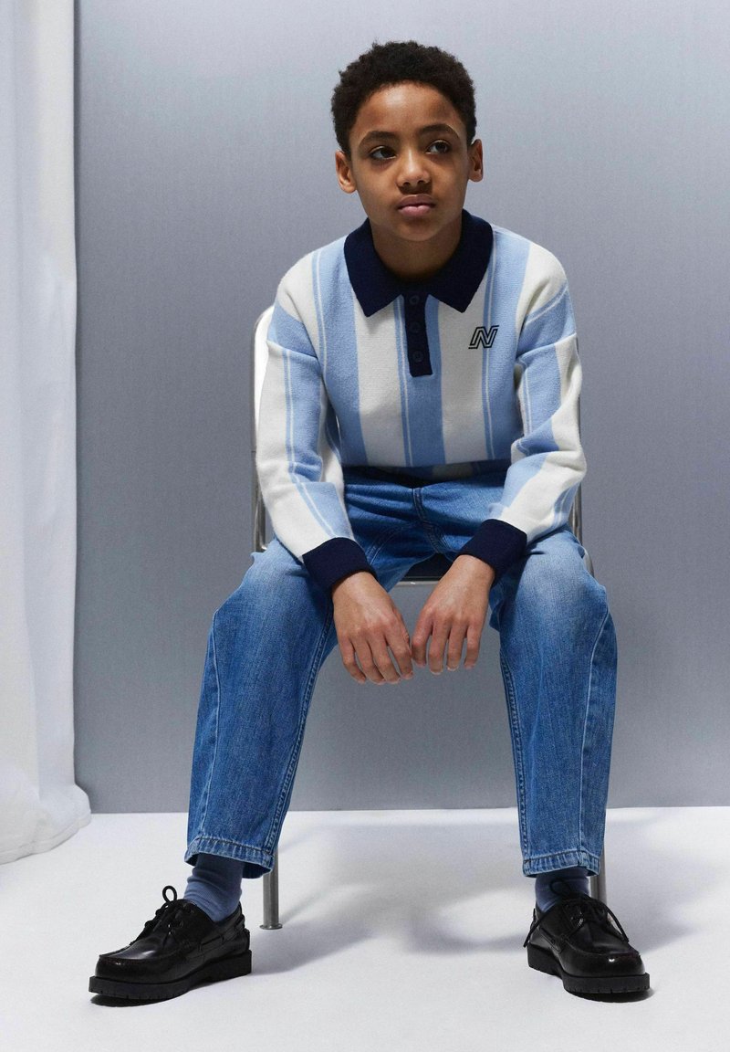 Ribadeega pullover helesinise ja valge triibuga, tumeda kraega, koos siniste teksade ja mustade nööbisaabastega. Lihtne, juhuslik disain.