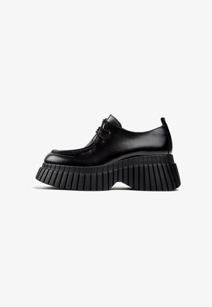 Chaussures à plateforme noires avec un dessus en cuir brillant, détails en dentelle et une semelle épaisse, nervurée. Bout rond et design à coupe basse.