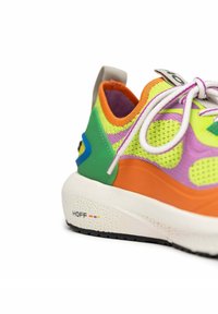 Colorful sneaker features mesh materials in green, pink, orange, and yellow. Thick white midsole with branding and textured accents.