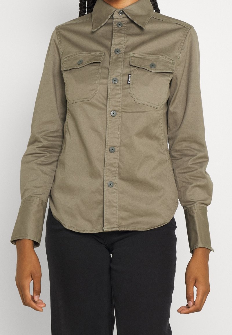 Olivgrön knapp-up skjorta med två bröstfickor, långa ärmar och rak nederkant, tillverkad av ett slätt tyg med en funktionell design.