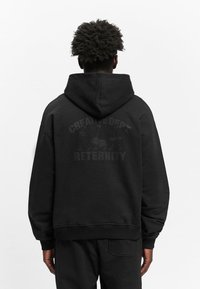 Black hooded sweatshirt made of soft fabric. Features a graphic print on the back with the text “CREATIVE DEPT. ETERNITY.” Loose fit, ribbed cuffs.