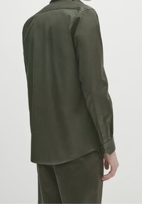 Camicia botton down verde scuro con colletto strutturato, maniche lunghe e orlo curvo. Realizzata in tessuto liscio, con una leggera lucentezza.