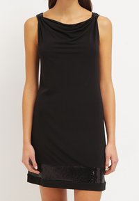 Svart ärmlös klänning med draperad halsringning, prydda axeldetaljer och en paljettkant. Tillverkad av ett mjukt, elastiskt tyg.
