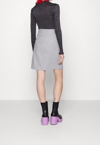Jupe grise en forme de A avec une texture lisse, associée à un haut noir pailleté à manches longues et des bottines noires à talons épais violets.