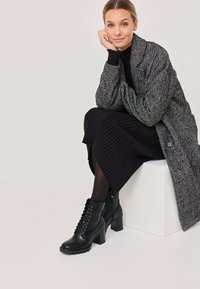 Stivaletti neri in pelle con dettagli in pizzo e tacchi chunky, abbinati a una gonna nera a coste e a un soprabito grigio testurizzato.