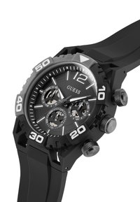 Orologio con cinturino in gomma nera, cassa nera opaca, numeri bianchi e tre quadranti secondari. Presenta una corona e pulsanti audaci e texturizzati.