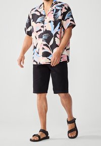 Short-sleeve button-up shirt with a black background, featuring pastel tropical leaf patterns. Paired with black shorts and black sandals.