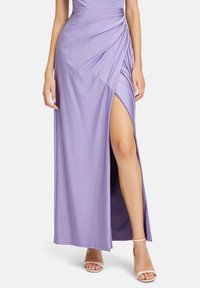 Lila Maxikleid mit drapiertem Design und einem hohen Schlitz bis zum Oberschenkel. Es besteht aus weichem Stoff und hat eine figurbetonte Silhouette, kombiniert mit nude-farbenen, strappy High Heels.