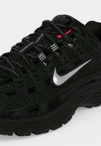 Μαύρο αθλητικό παπούτσι Nike με παχιά σόλα, ασημένιο λογότυπο swoosh, διαπνέον σχέδιο από δίχτυ και μαύρα κορδόνια με ανακλαστικές τελείες.