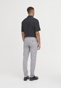 Sort polo shirt, grå bukser med slim fit, set bagfra, glat stof, to baglommer med knapper, kombineret med sorte sko.