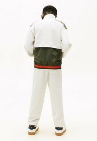 Felpa grigia con sezione inferiore verde oliva e cintura elastica rossa, abbinata a pantaloni grigi chiari e sneaker bianche con dettagli blu navy.