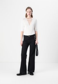 Pantalons larges noirs avec des accents de boutons dorés associés à un haut blanc avec un décolleté en V profond et des manches courtes. Texture de tissu lisse.