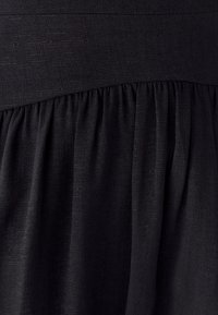Black fabric with visible texture and gathered pleats creating a layered, slightly flared effect.