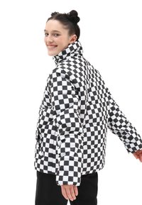 Giubbotto imbottito con motivo a scacchi nero e bianco, colletto alto e tasche laterali. Realizzato in materiale trapuntato e imbottito per garantire calore.