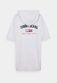 Světle šedá oversized mikina s kapucí, která má přední klokaní kapsu a vyšitý text "TOMMY JEANS NEW YORK CITY" v námořnické modři a červené.