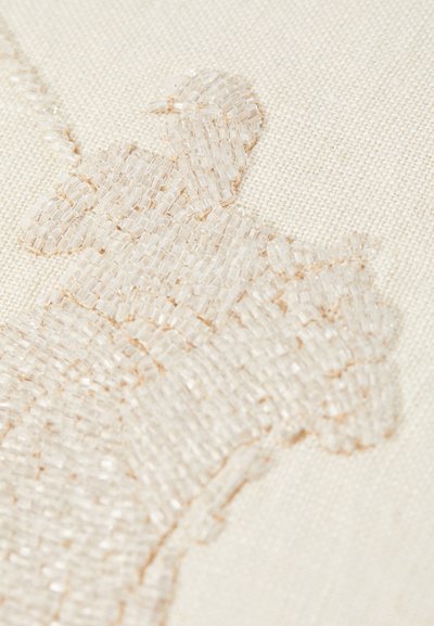 Beaded textile art featuring a subtle white-on-white design with a textured, raised surface on a light beige fabric background.
