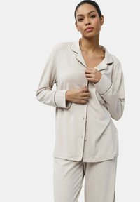 Ensemble de pyjama beige clair comprenant un haut à boutons avec col à revers et manches longues, associé à un pantalon assorti en tissu doux et lisse.
