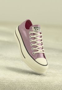 Converse All-Star tenisice od sjajne ružičaste tkanine, s bijelim vezicama, gumenim vrhom i crnom etiketom na jeziku.