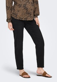 Jeans en denim noirs à coupe slim, associés à des sandales à glisser en cuir marron. Le haut présente un motif léopard avec des manches bouffantes.