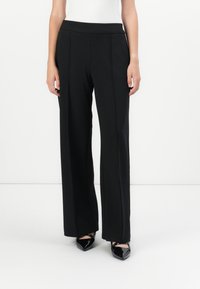 Zwarte wijde broek met een gladde textuur, voorzien van een hoge tailleband en minimale stikdetails, gecombineerd met zwarte puntige hakken.