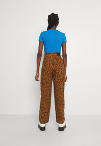 Blå ribbad kortärmad t-shirt ihop med bruna högmidjade byxor med leopardmönster och svarta detaljer. Vita platåstövlar.