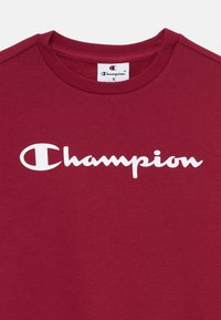 Bordeaux bomull T-skjorte med rund hals, med en stor hvit "Champion"-logo over brystet. Myk tekstur og standard passform.