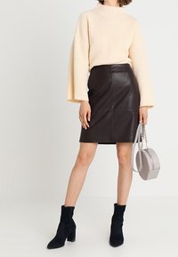 Beige ribbed neulepaita, jossa on kellottuvat hihat, yhdistettynä istuvaan ruskeaan nahkahameeseen. Mustat samettiset nilkkurit ja pyöreä hopeinen laukku viimeistelevät asun.