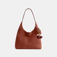 Sac à épaule en cuir marron avec une bandoulière unique et un pendentif cerise accroché sur le côté, devant un fond uni.