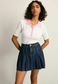 Weißes geripptes Strickoberteil mit rosa Gingham-Kragen und Knöpfen; kombiniert mit einem dunkelblauen A-Linien-Rock mit Falten und ausgefranstem Saum.