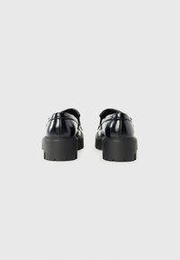 Black leather shoes with a glossy finish, rounded toe, and thick textured sole. Minimalistic design with back strap detail.