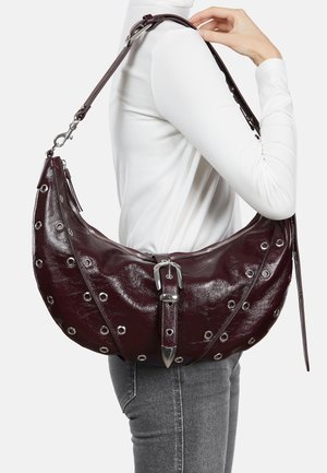 Burgundy leather shoulder bag with silver grommets, zip closure, buckle detail, and adjustable strap; curved hobo shape, glossy texture.