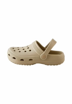 Beige slip-on clog with ventilation holes, textured sole, and adjustable heel strap, designed for casual wear and comfort.