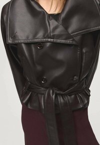 Czarny skórzany płaszcz trench z szerokim kołnierzem, podwójnym zapięciem z przodu, paskiem w talii oraz gładką teksturą. Widoczne guziki i kieszenie.