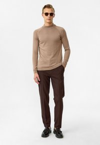 Lichtbruine fitted trui met een hoge hals, gecombineerd met donkerbruine op maat gemaakte broek en zwarte veterschoenen. Romige textuur door het geheel.