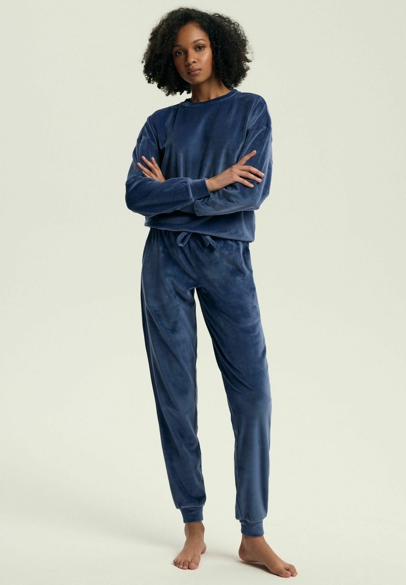 Granatowy welurowy zestaw wypoczynkowy z długim rękawem, z okrągłym dekoltem oraz dopasowanymi spodniami dresowymi ze sznurkiem w pasie i ściągaczami na nogawkach.